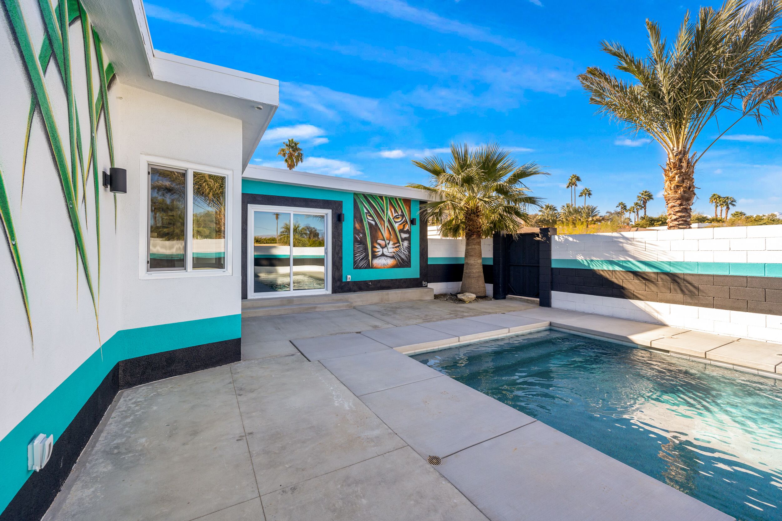 Una casa moderna con piscina, palmeras y un cielo azul despejado.