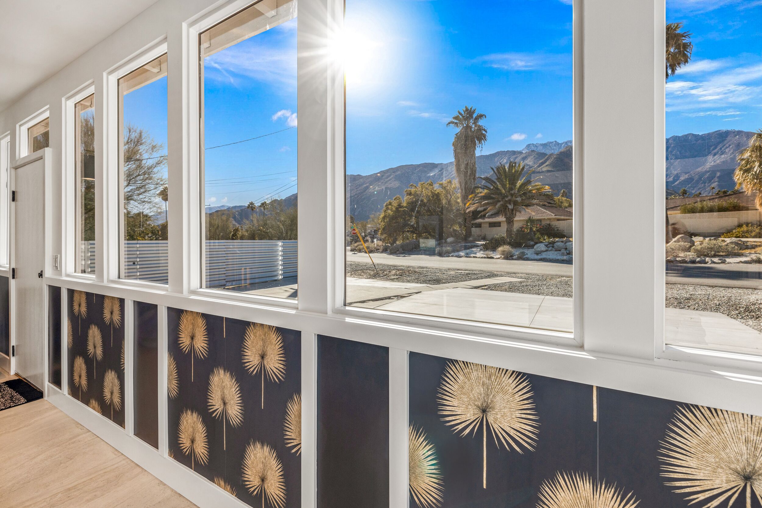 A room with large windows offering a view of mountains and palm trees.