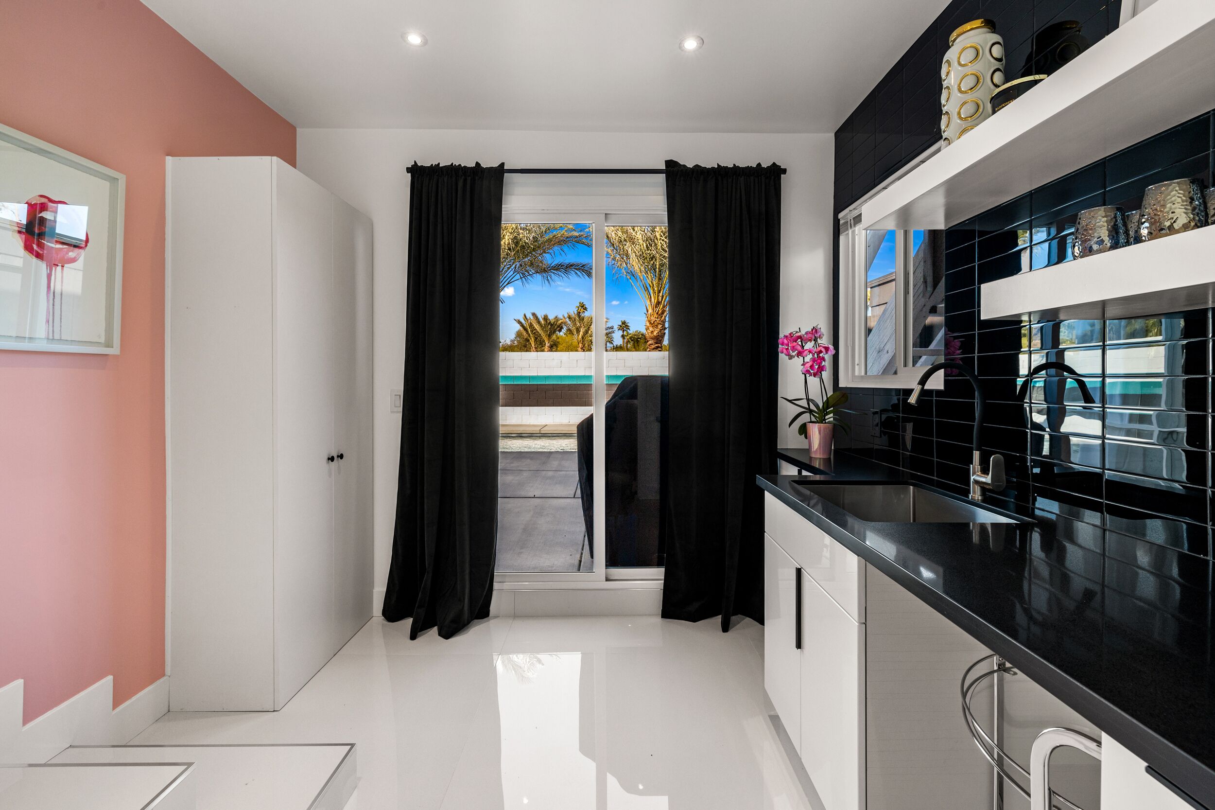 A modern kitchen with black countertops, white cabinets, and a view of palm trees through the sliding glass door.