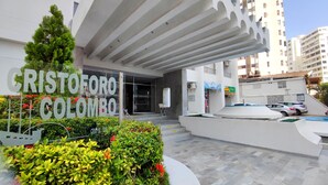 A modern building with a prominent entrance, a sign reading "CRISTOFORO COLONBO," and a parking area with cars. - Beautiful Apartment in Bocagrande  (Cartagena)