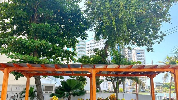 An outdoor seating area with a wooden pergola, cushioned chairs, and potted plants. - Beautiful Apartment in Bocagrande  (Cartagena)