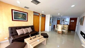 A modern living room with a sofa, coffee table, and ottoman. There is a dining area with chairs and a table. The room has wooden walls and a painting on the wall. - Beautiful Apartment in Bocagrande  (Cartagena)
