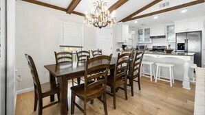 Une cuisine moderne avec des meubles blancs, un îlot central doté de tabourets et un lustre.