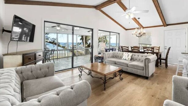 Un salon spacieux avec un grand canapé, une table basse et un téléviseur. Il y a un balcon avec vue sur la mer.