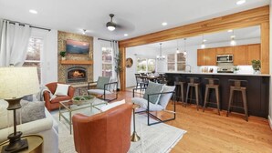 Una sala de estar moderna con chimenea, zona de estar y cocina con armarios de madera y taburetes de bar.