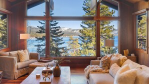 L’intérieur chaleureux d’un chalet, avec de grandes fenêtres donnant sur un lac et une forêt.
