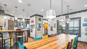 Un vaste espace dédié à la salle à manger, avec une longue table en bois, des chaises colorées et des luminaires suspendus.