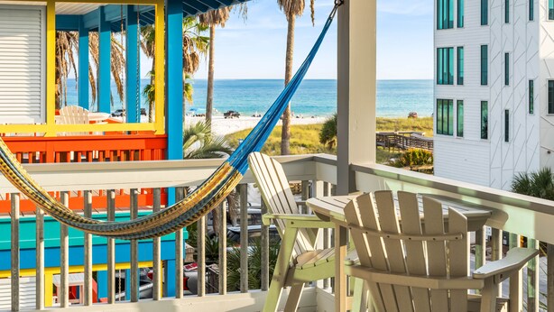 Un balcon avec un hamac, une vue sur la plage et un immeuble à la façade colorée.