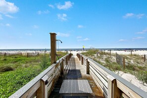 A wooden boardwalk leading to a beach with a metal grate at the end.
