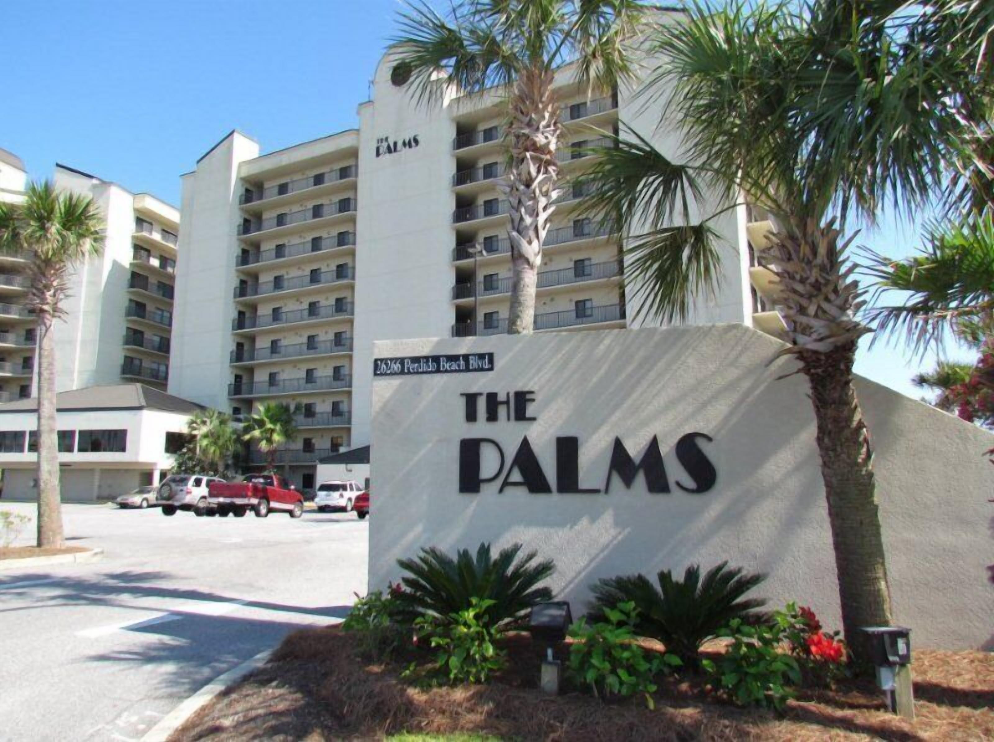 A sign for The Palms hotel with a multi-story building in the background.