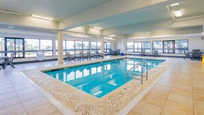 Une piscine intérieure à l’eau d’un bleu limpide, entourée de chaises et dotée d’un sol carrelé.