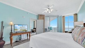 Une chambre dotée d’un grand lit, d’un ventilateur de plafond, d’une télévision et offrant une vue sur l’océan grâce à une porte coulissante.
