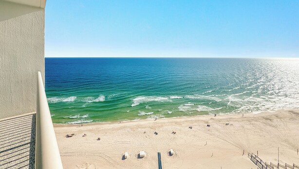 A beach view from a balcony with a clear sky, sandy beach, and ocean waves. - Palacio 1703 | Stunning Gulf Views | My Beach Getaways (Pensacola)