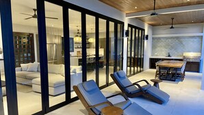 A modern living area with a glass wall, lounge chairs, a wooden table, and a kitchen area with a grill. - Outstanding High End Luxury, Most Convenient Location and World Class Ocean View (Uvita)