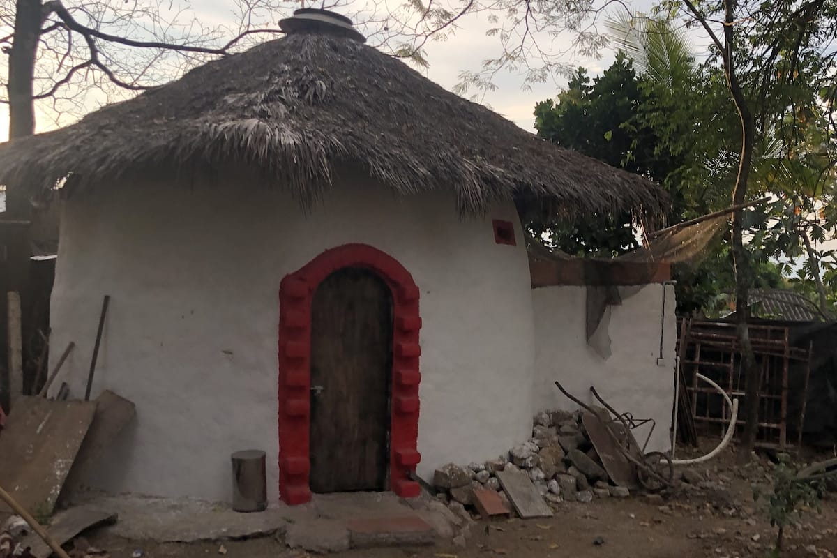 Un edificio pequeño de una sola planta con techo de paja y puerta de marco rojo.