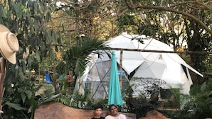 Um grupo de pessoas sentadas num banco de madeira num jardim, com uma grande tenda branca ao fundo.