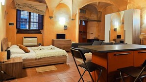 Un dormitorio con cama, escritorio, silla, una mesita y una pequeña cocina.