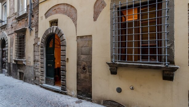 Una calle empedrada con un edificio que presenta un arco de entrada y una ventana con rejas.