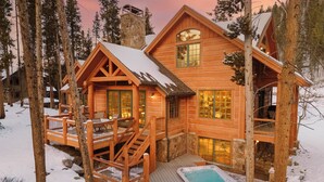 Una cabaña de troncos con terraza, jacuzzi y chimenea de piedra.
