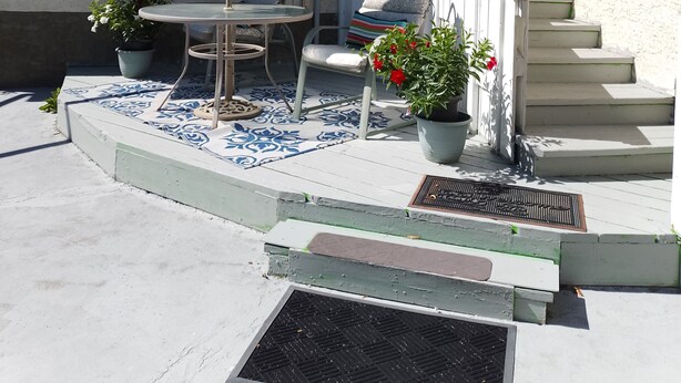 Un patio con una mesa y sillas, una planta en maceta y una escalera que lleva a la entrada.