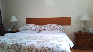 Una cama bien hecha con ropa de cama floral, dos lámparas de noche y una mesita de noche de madera con una lámpara.