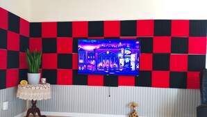 Una habitación con un televisor montado en la pared, paneles acústicos rojos y negros, una mesita con una planta, una girafa decorativa y suelo de madera.