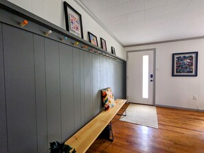 Un pasillo con un banco de madera, una pared gris con ganchos y obras de arte enmarcadas.