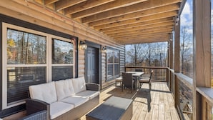 Eine überdachte Holzterrasse mit Sitzgelegenheiten im Freien, darunter eine Couch und Stühle sowie ein Tisch.