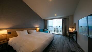 A hotel room with a large bed, a desk with a chair, a small table, and a balcony with a view.
