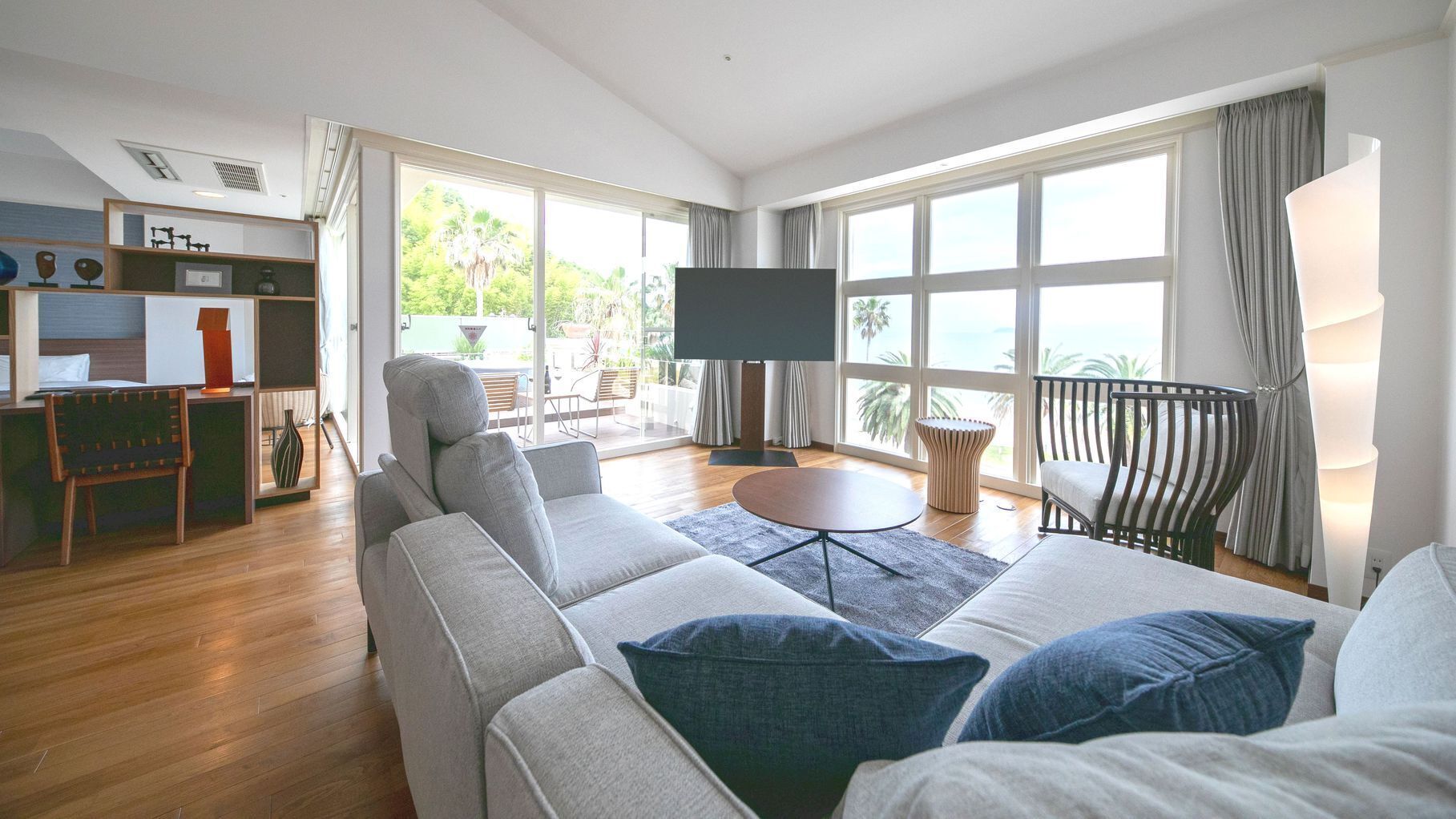 A modern living room with a sofa, a TV, and a balcony with a view.