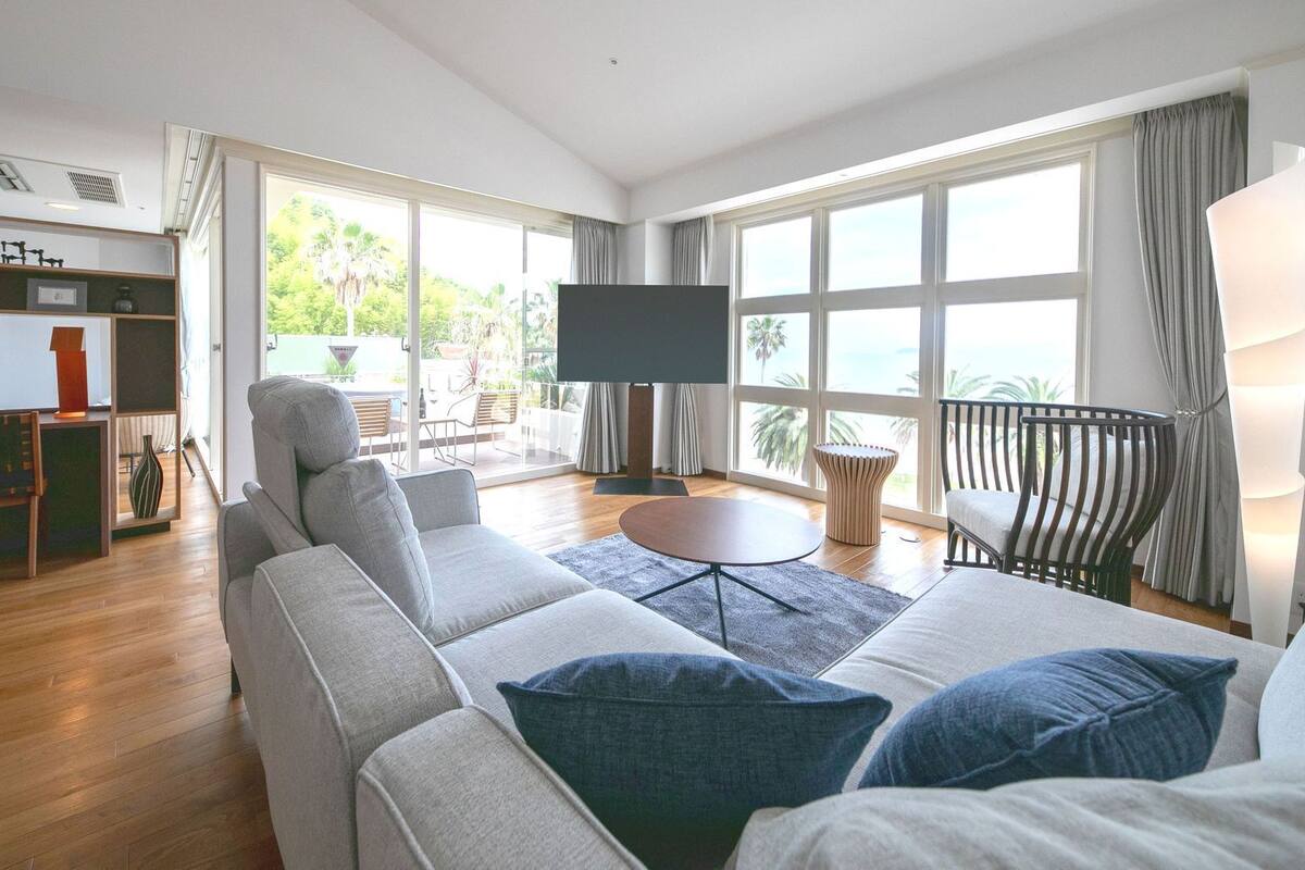 A modern living room with a sofa, a TV, and a balcony with a view.