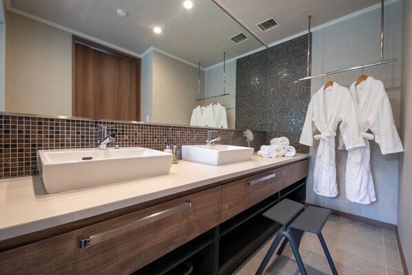 A modern bathroom with two sinks, a large mirror, and a towel rack with robes.