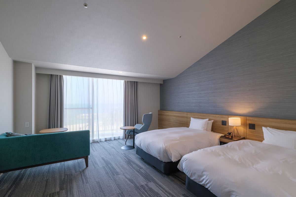 A hotel room with two beds, a sofa, a small table, and a chair.