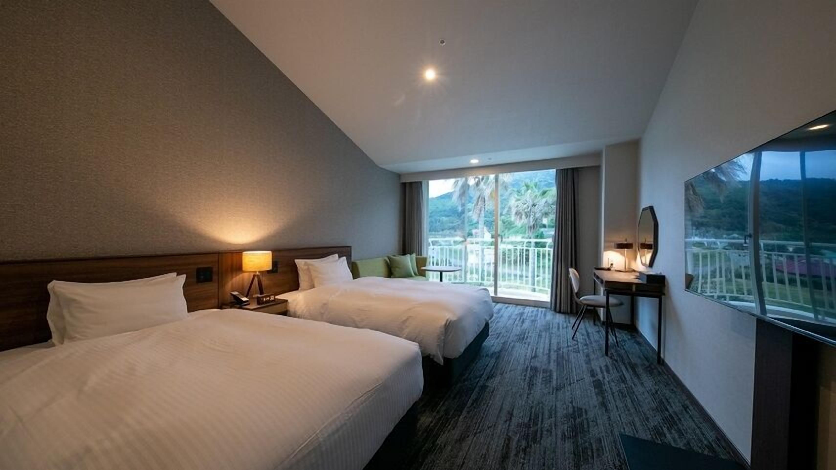 A hotel room with two beds, a desk, a chair, a balcony with a view, and a large window.