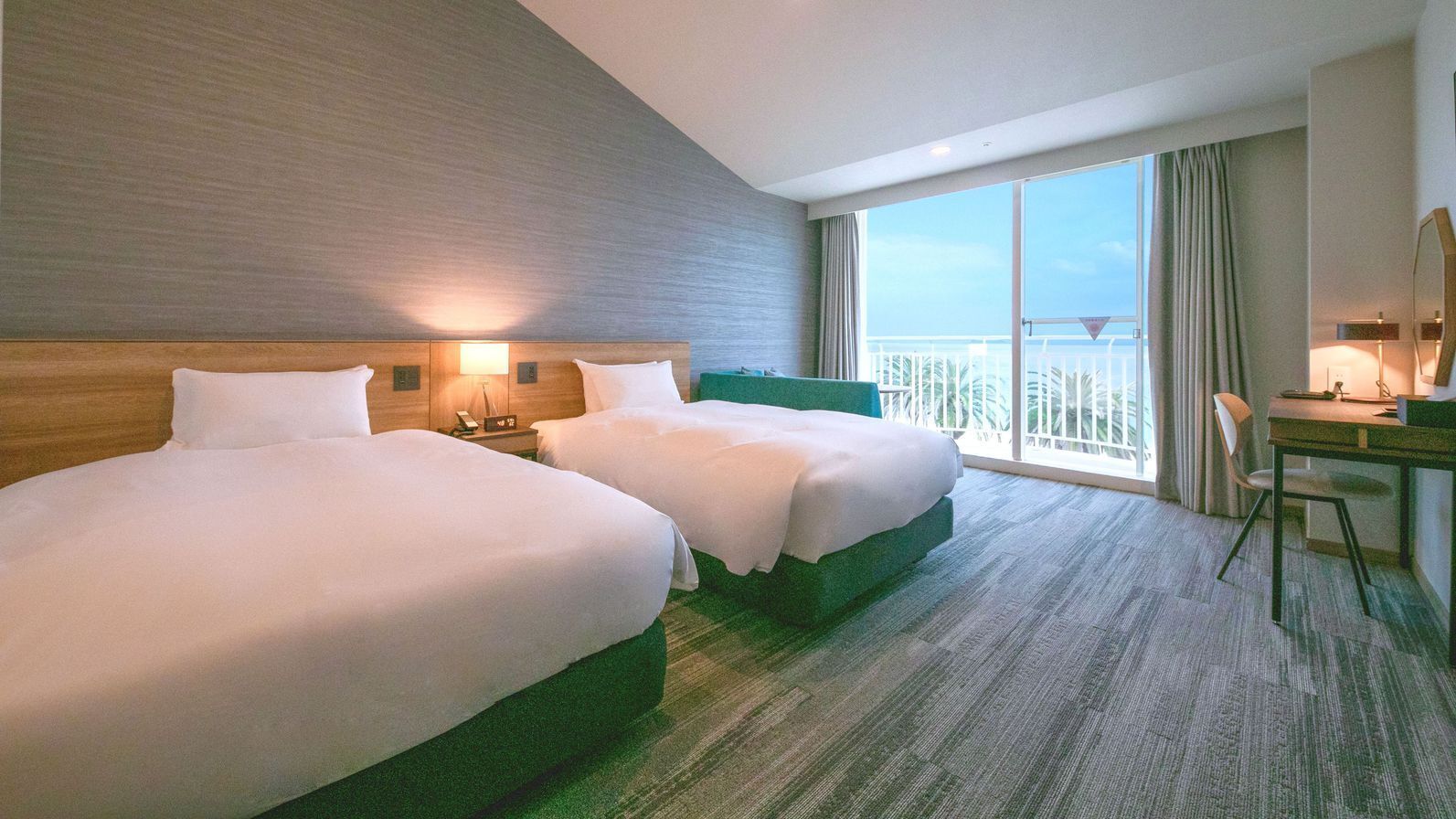 A hotel room with two beds, a desk, a chair, and a large window with a balcony view.