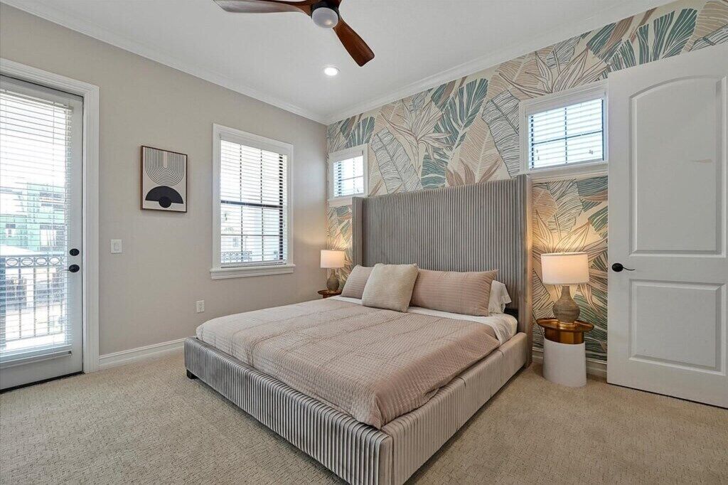 A bedroom with a bed, a ceiling fan, two bedside lamps, and a door.