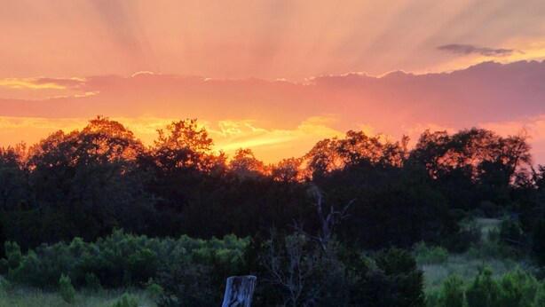 A sunset over a forested area with a wooden fence in the foreground. - Primitive Camping⛺️Under the Stars🌠 
5 minutes to Bandera! (Bandera)