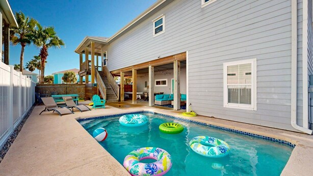 Ein Schwimmbecken mit Schwimmreifen, eine überdachte Terrasse mit Stühlen und ein Holzdeck.