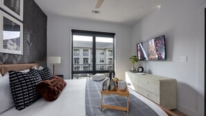 A modern hotel room with a bed, a TV, a window, and a view of buildings.