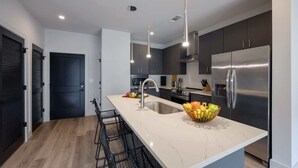 A modern kitchen with a marble countertop, stainless steel appliances, and black bar stools.