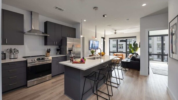 A modern kitchen with a central island, bar stools, and a dining area with a sofa.