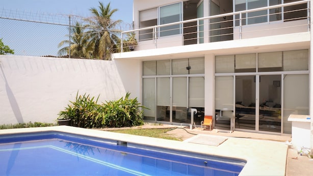 Um edifício moderno com grandes janelas, piscina e área cercada com plantas.