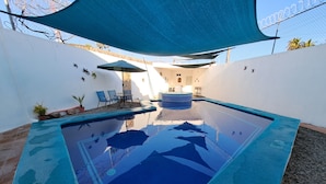 Uma piscina com toldo azul, cercada por paredes brancas e vasos de plantas.
