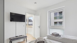 Een moderne slaapkamer met een bed, een bankje, een televisie en een raam met zonwering.