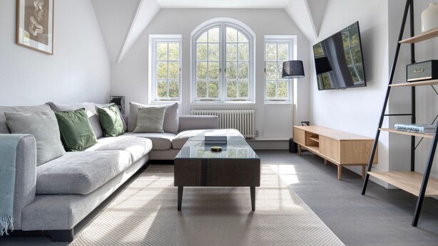 A modern living room with a grey sofa, a glass coffee table, a wooden TV stand, and a radiator. - Serene St Johns Wood 2BR, nr Park & Universities, by Blueground (London)