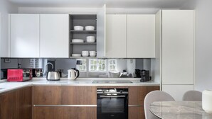 A modern kitchen with white cabinets, a wooden countertop, a built-in oven, and a dining area with a glass table and chairs. - Serene St Johns Wood 2BR, nr Park & Universities, by Blueground (London)