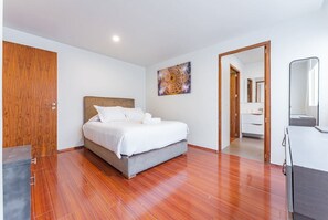 Ein Schlafzimmer mit einem Bett, Holzboden, einer Holztür, einem Gemälde und einem Spiegel.