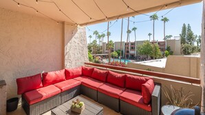 A balcony with a red sectional sofa, a small table with a plant, and a view of a pool and palm trees. - Maya Motel (Scottsdale)