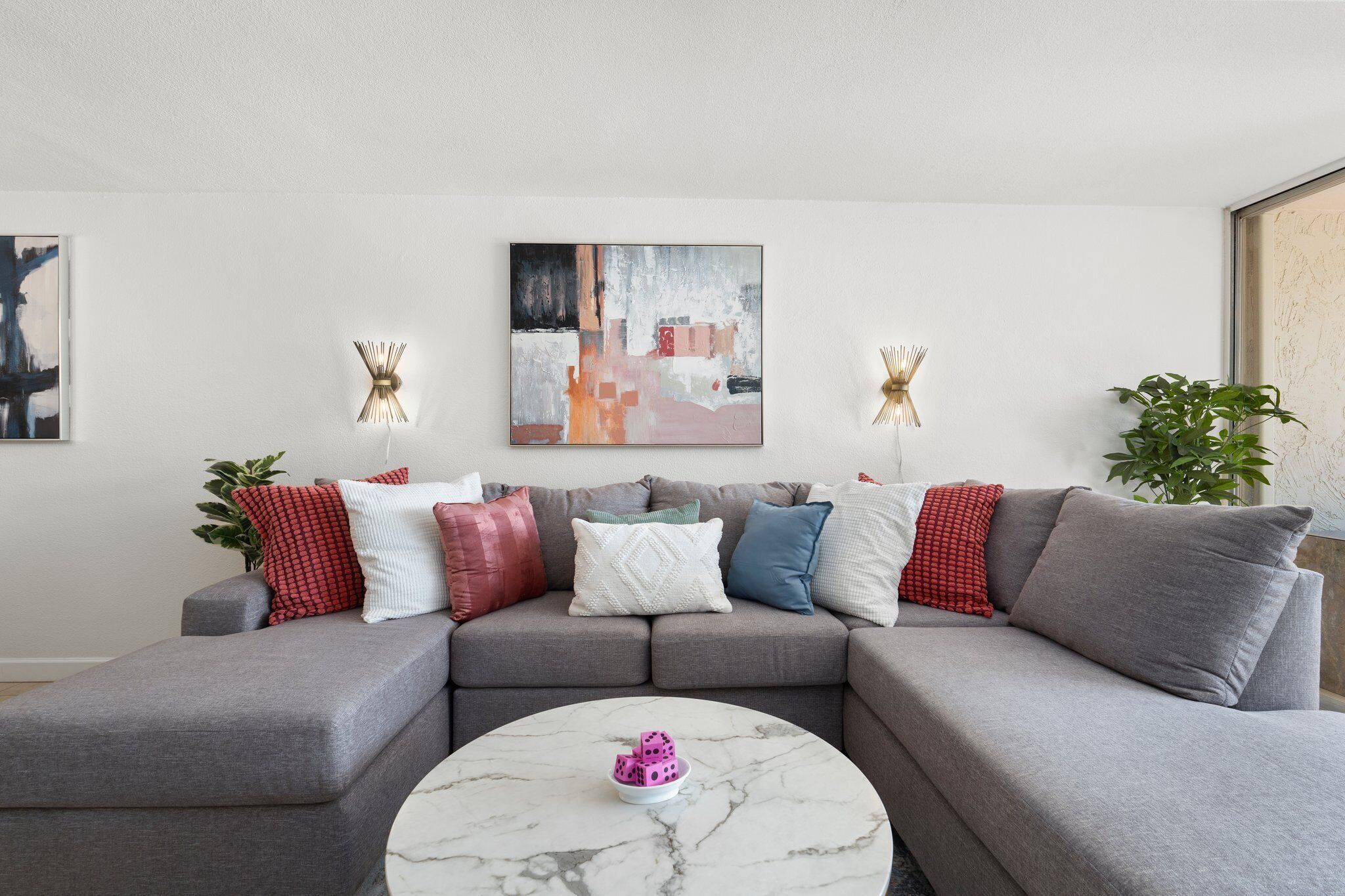 A modern living room with a grey sectional sofa, a marble coffee table, and a contemporary abstract painting on the wall.