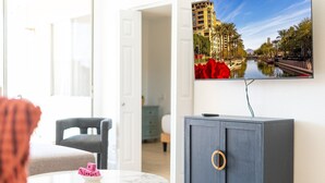 A modern living room with a grey cabinet, a round door, and a flat-screen TV mounted on the wall displaying a cityscape. - Maya Motel (Scottsdale)